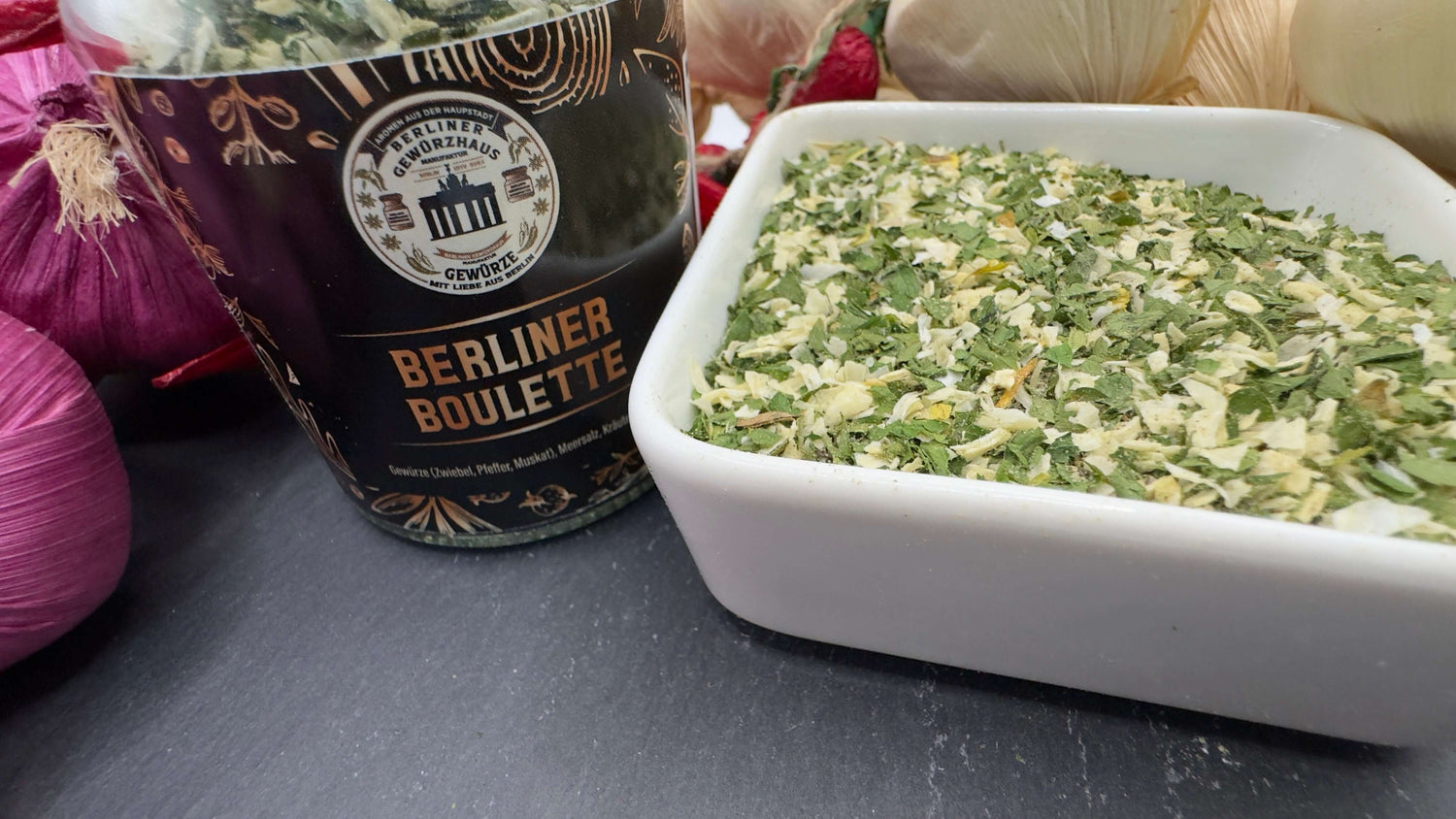 Berliner Boulette Gewürzzubereitung in einer Schale mit frischen Kräutern und Zwiebeln im Hintergrund.