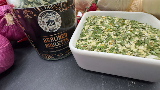 Berliner Boulette Gewürzzubereitung in einer Schale mit frischen Kräutern und Zwiebeln im Hintergrund.